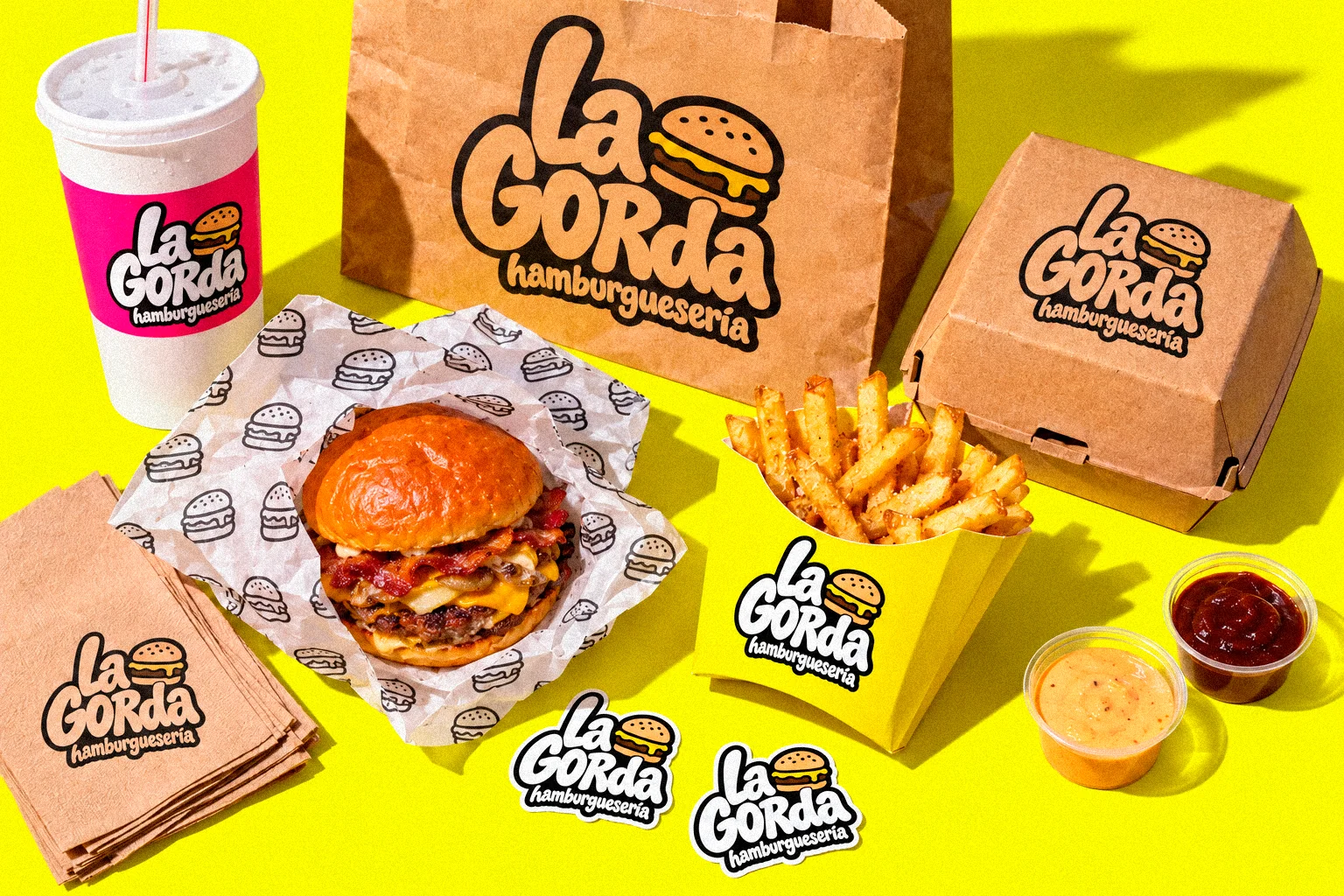 Vaso, bolsa, caja, papel, patatas y pegatinas de La Gorda sobre fondo amarillo